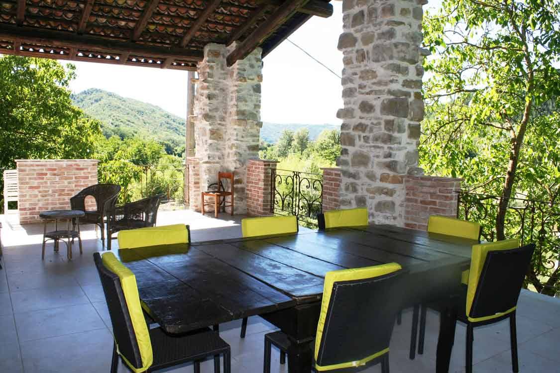 Tavolo in legno con sedie nere e gialle sotto pergolato di pietra