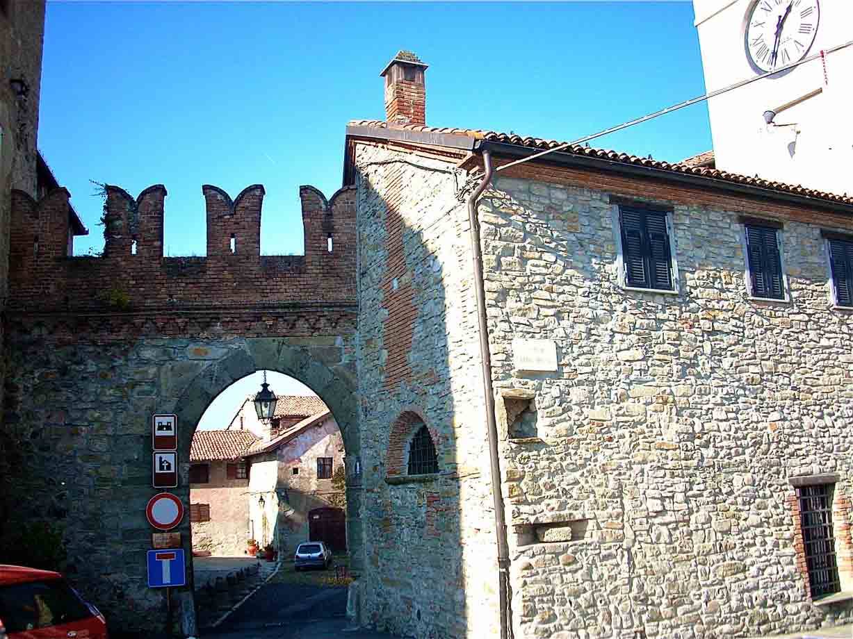 Porta medievale in mattoni con merli, case in pietra e torre con orologio