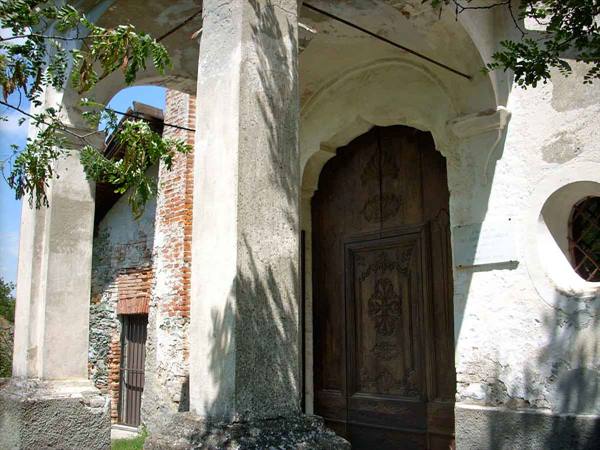 Carved wooden doorway beneath a porch with weathered stone columns and plaster