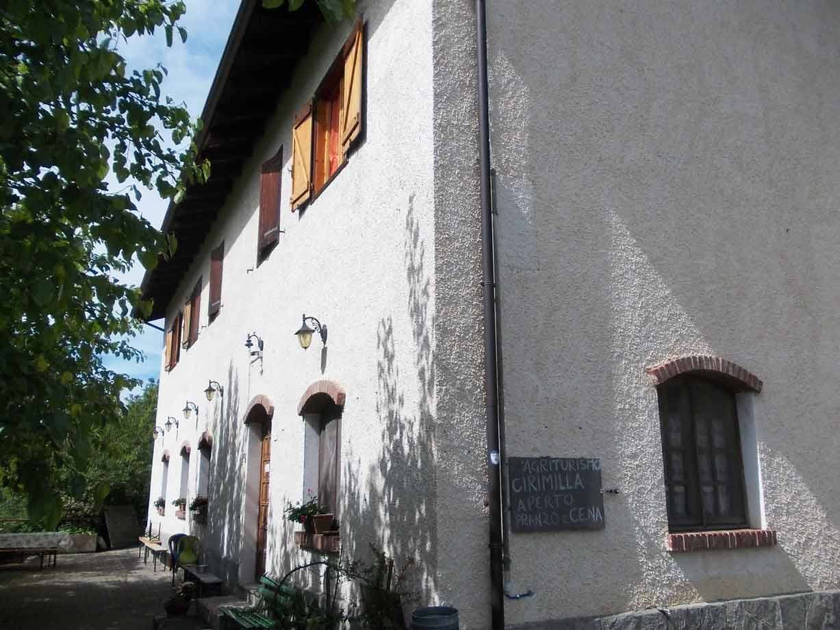 Facciata intonacata di agriturismo con persiane arancioni e insegna scritta a gessetto