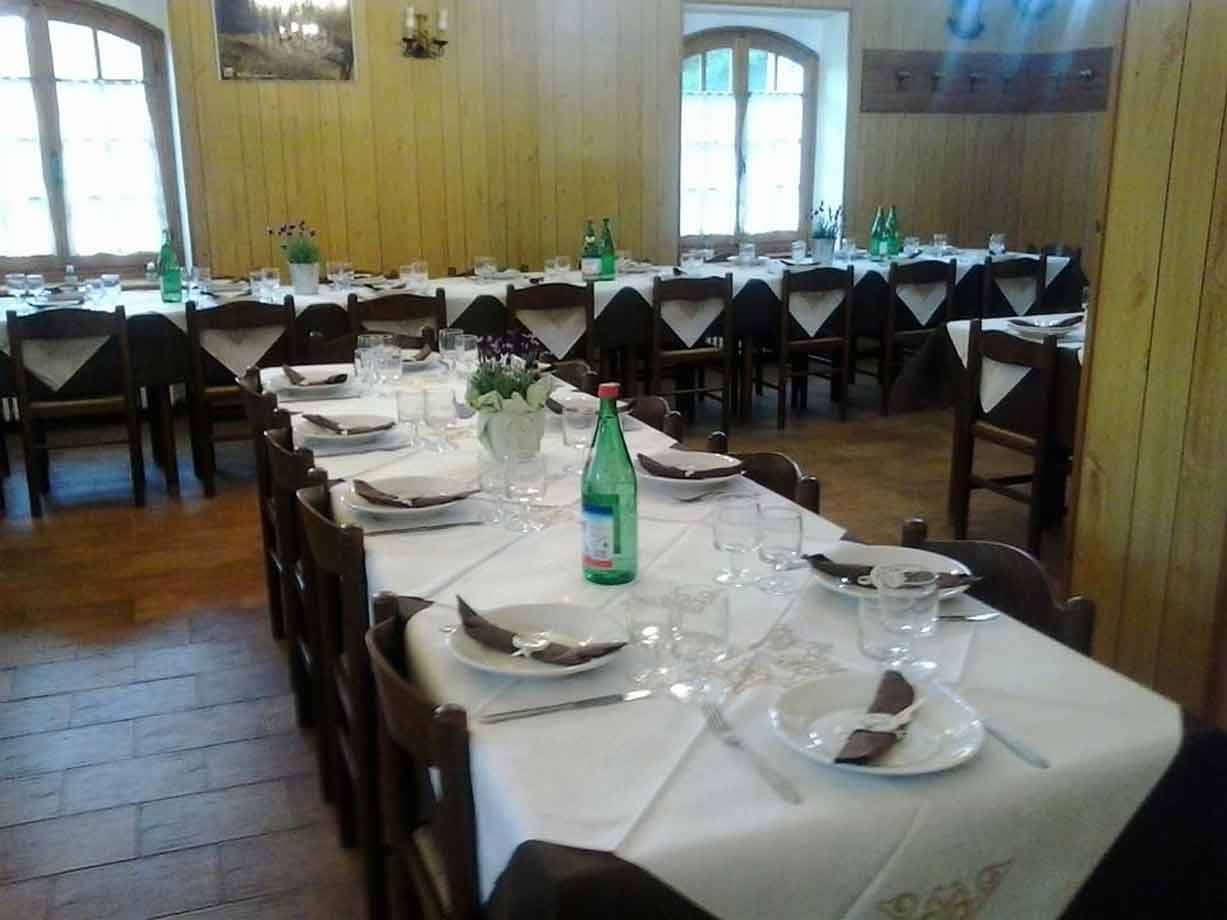 Sala di rifugio di montagna con tavoli apparecchiati a tovaglia bianca e bottiglie verdi