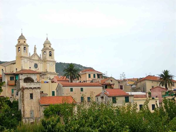 Baroque church with twin bell towers above terracotta roofs and palms, Liguria