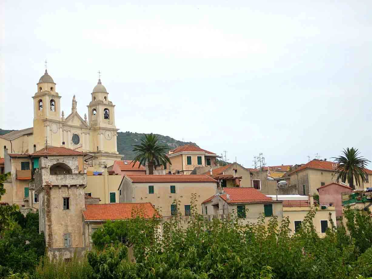 Chiesa barocca con due campanili sopra tetti terracotta e palme, Liguria