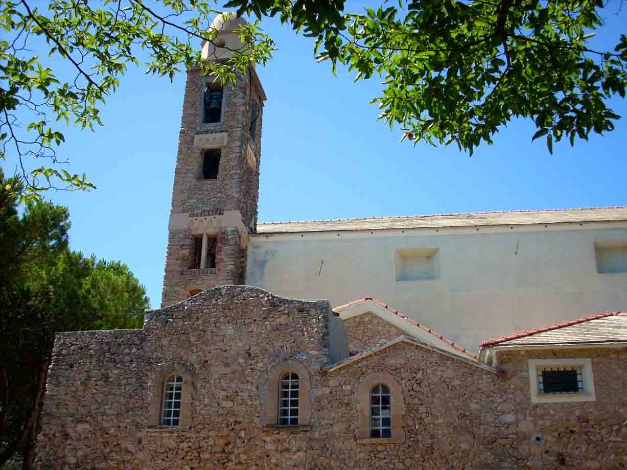 Campanile in pietra e chiesa bianca incorniciati dai rami verdi, cielo azzurro