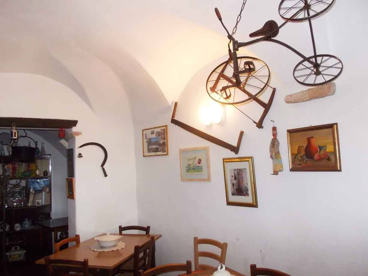 Sala con volta bianca, vecchia bicicletta appesa al soffitto, tavolo in legno