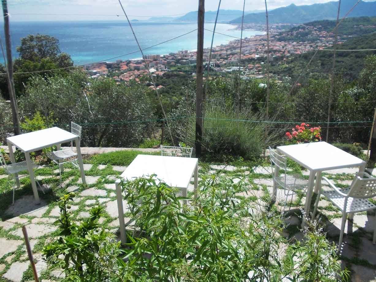 Tavolini bianchi su terrazza in pietra, città costiera e mare turchese