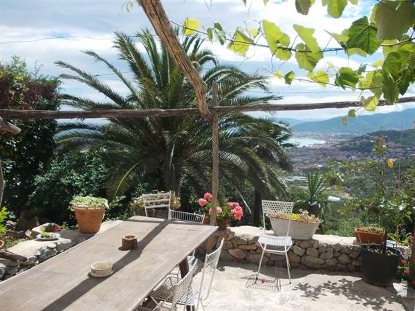 Wooden table on terrace with palms and vines, bay and town beyond