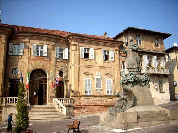 Bronze statue in front of brick building with Italian flags, sunny square