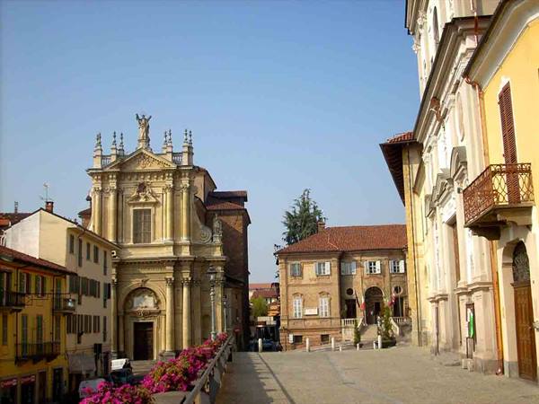Baroque church square with yellow palaces, pink flowers in foreground