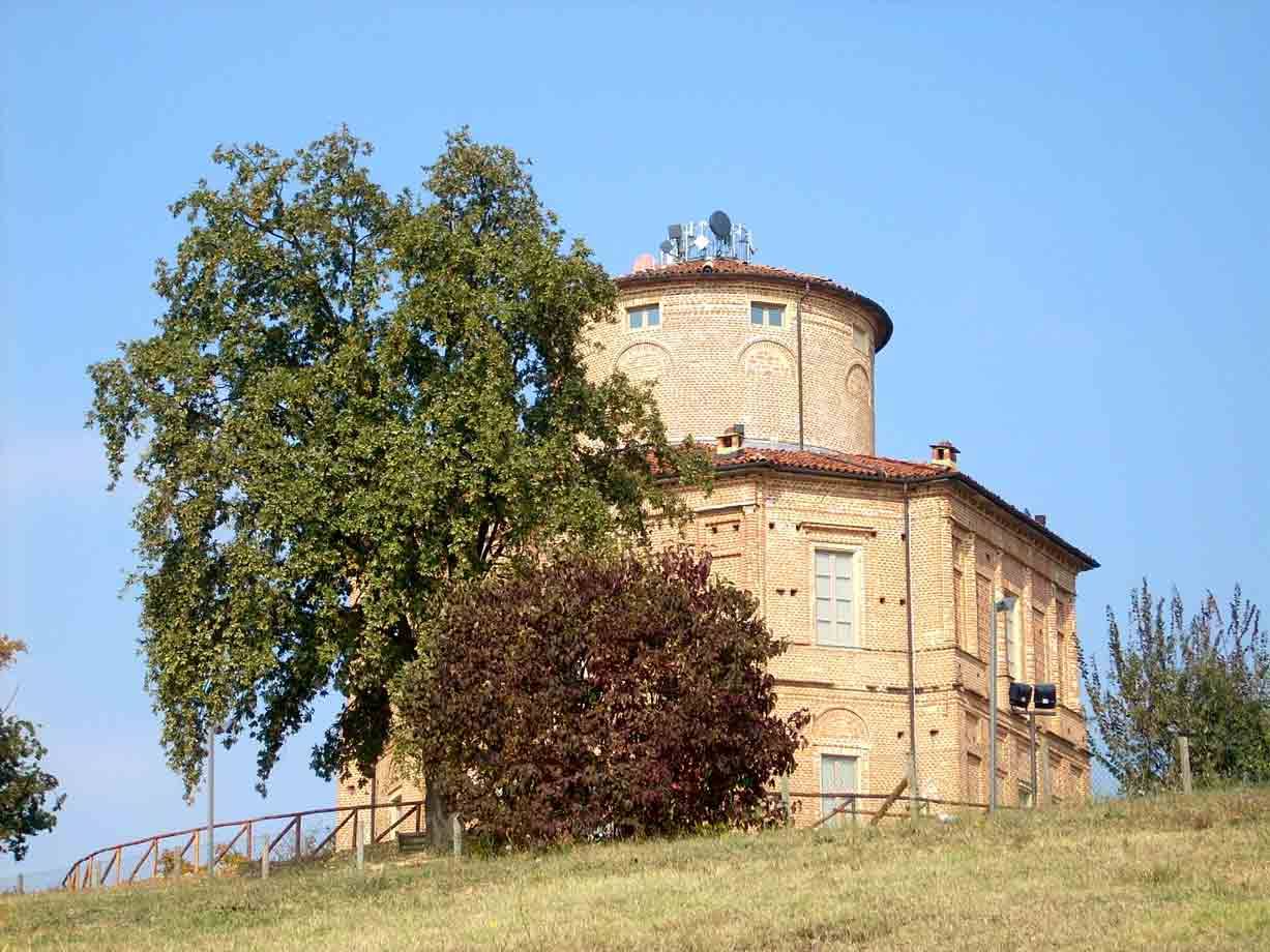 Antica casa rotonda in mattoni su collina erbosa, alberi autunnali e cielo azzurro
