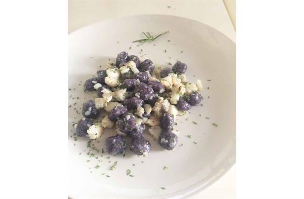 Purple gnocchi with cheese and parsley on white plate, rosemary sprig