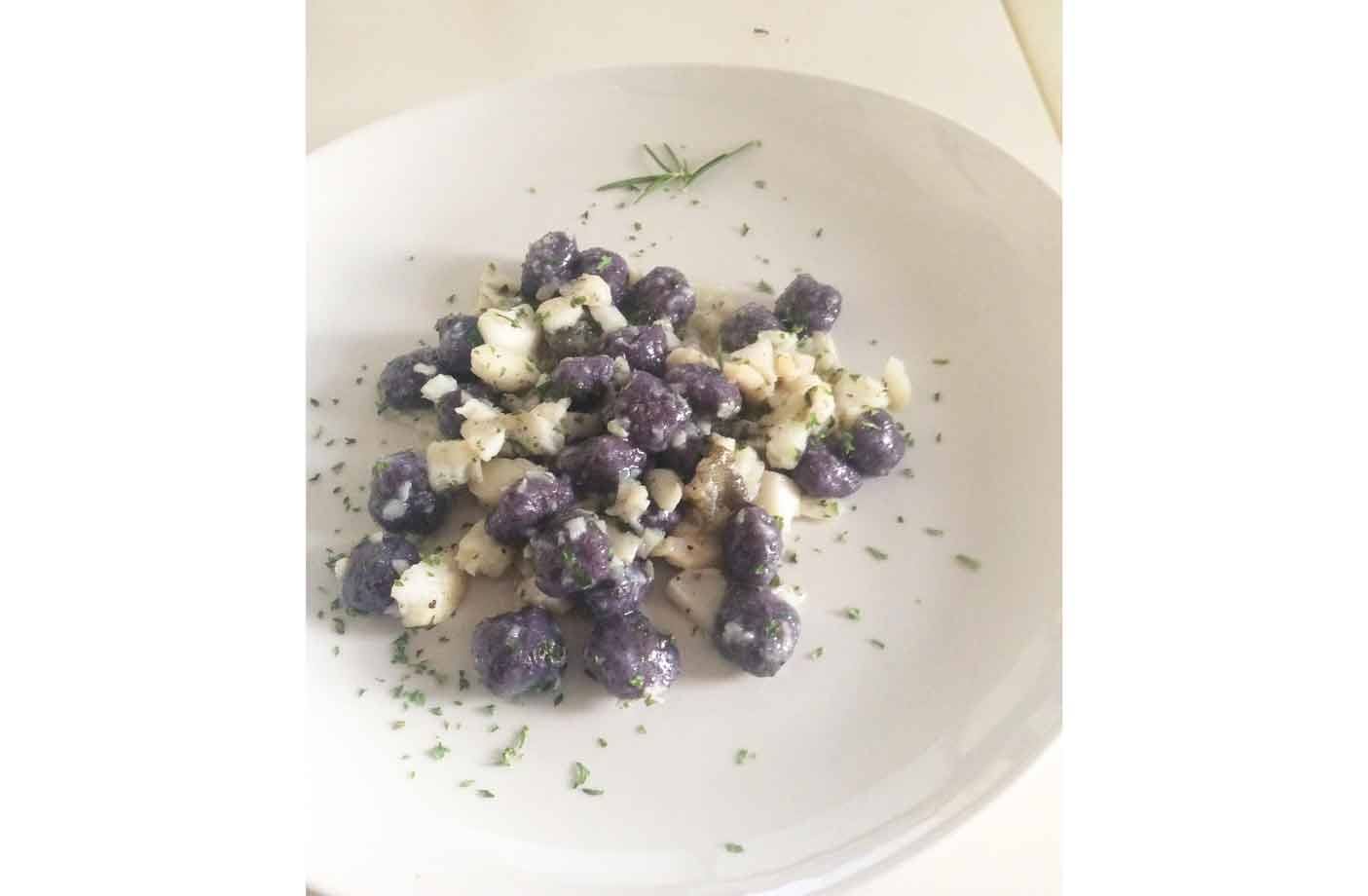 Gnocchi viola con formaggio e prezzemolo su piatto bianco, rametto di rosmarino