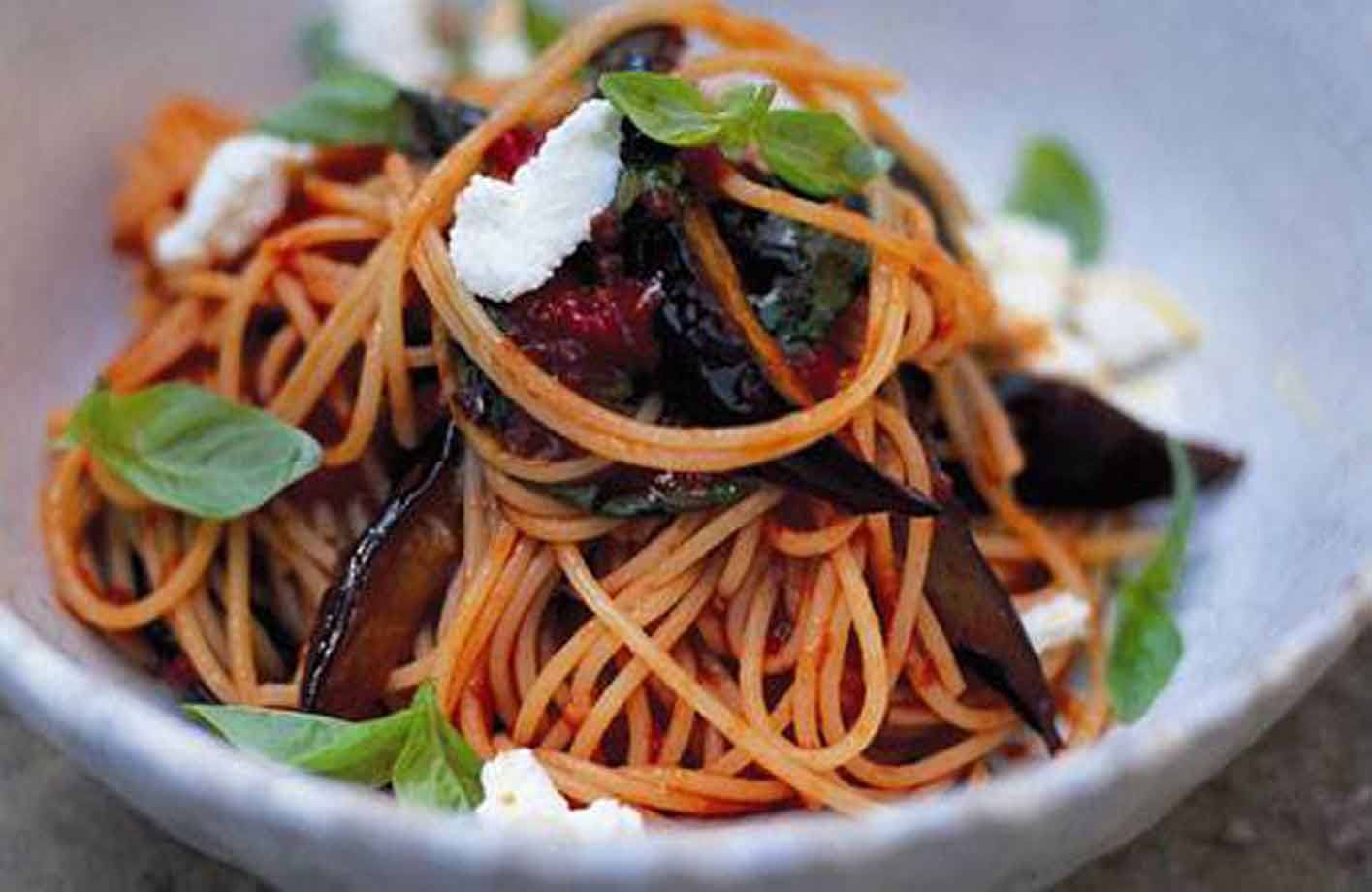 Spaghetti al pomodoro con melanzane, basilico e ricotta in ciotola bianca