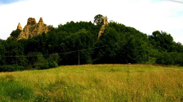 Clay badlands rising above green woods and a sunny grassy meadow