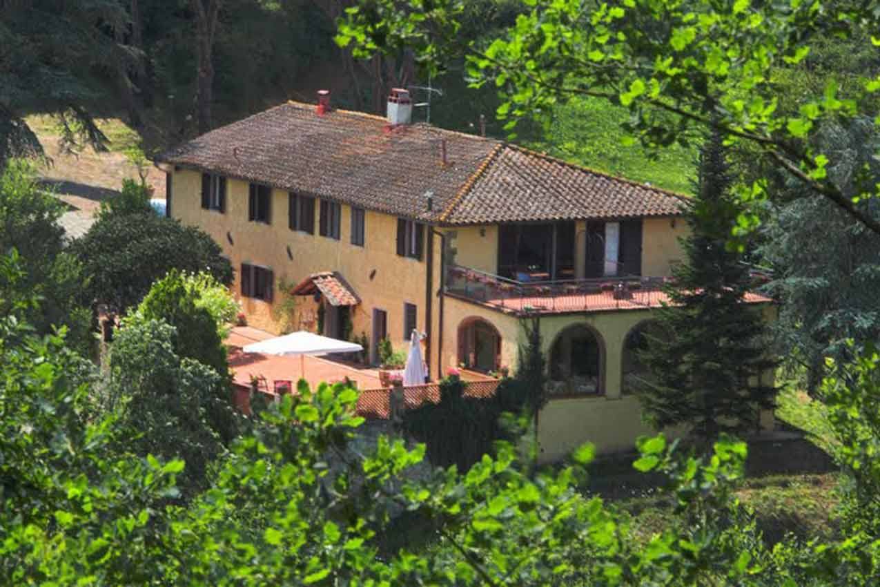 Casolare giallo con tetto in cotto tra gli alberi, terrazza con ombrellone