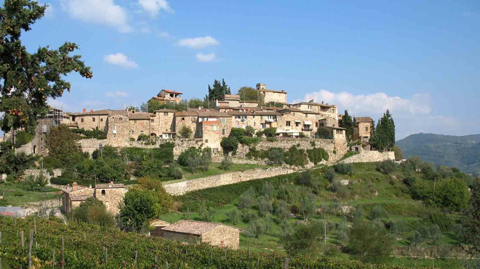 Borgo medievale di pietra sul colle, case di pietra, vigneti e ulivi sotto cielo azzurro
