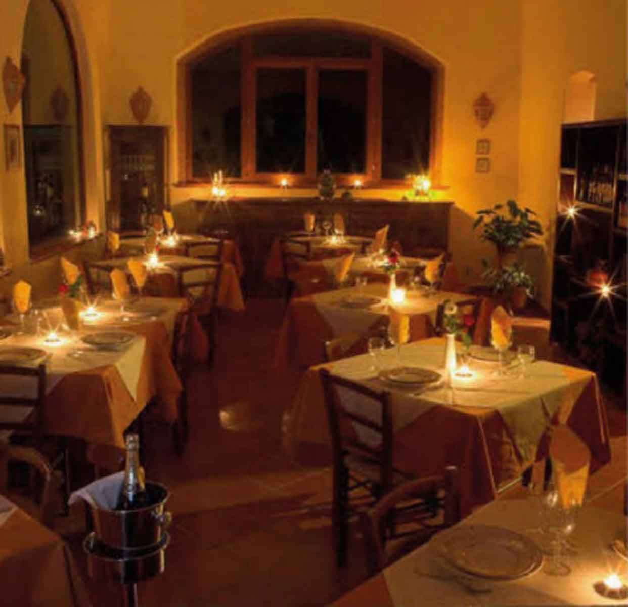 Sala di ristorante con tavoli apparecchiati, tovaglie arancioni e candele accese