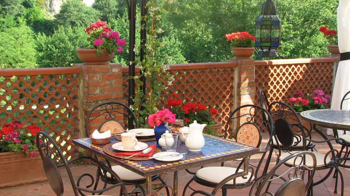Tavolo con ceramiche e fiori su terrazza in mattoni tra gerani