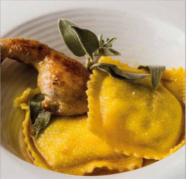 Golden ravioli with sage butter and roasted drumstick in white bowl