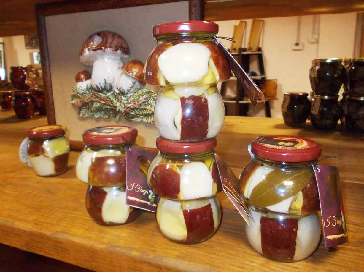 Barattoli di vetro con funghi sott'olio in negozio, luce calda su tavolo di legno