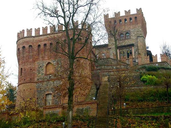 Brick castle with battlements and tower, stairs among autumn trees under grey sky