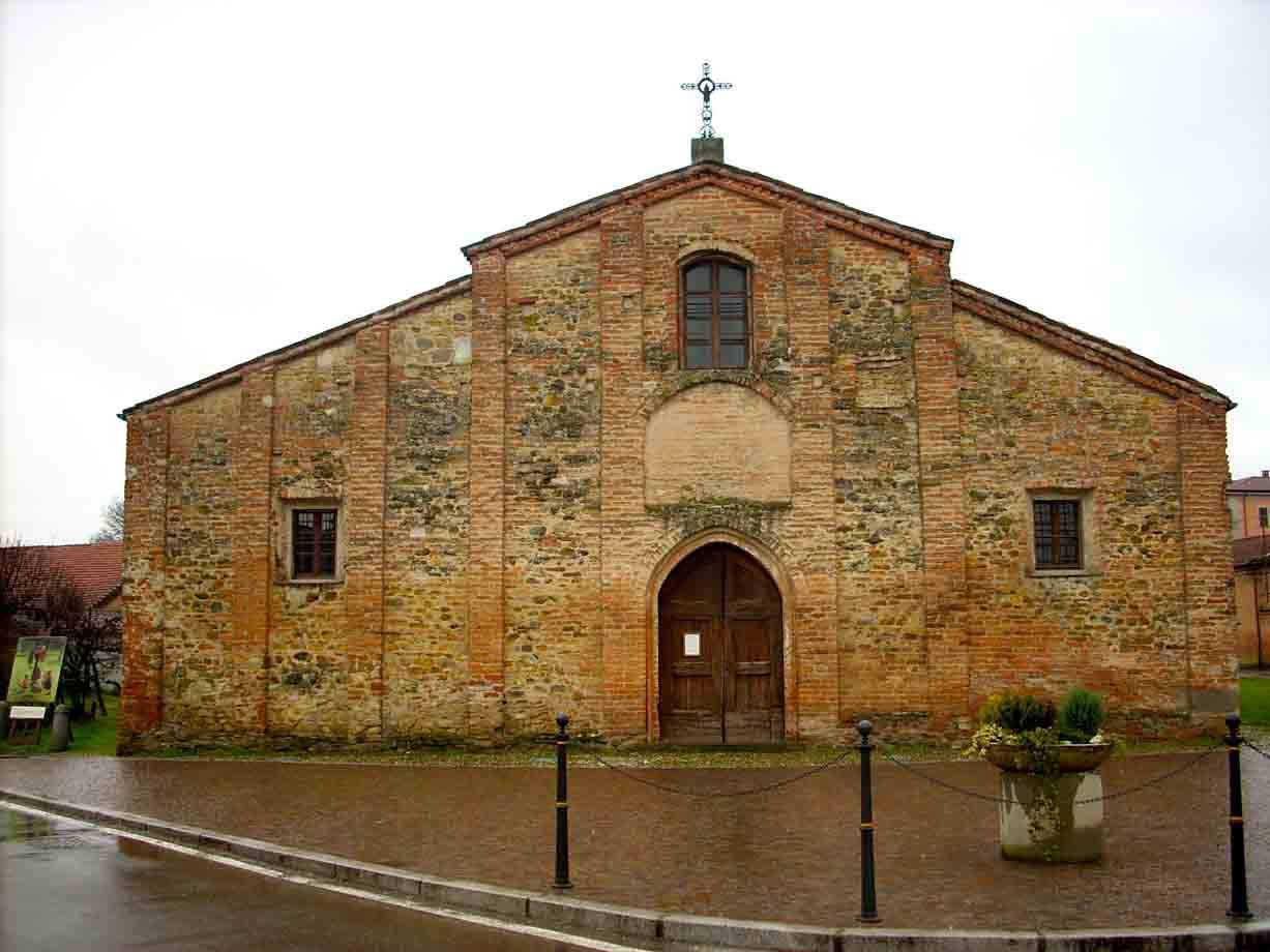 Chiesa in mattoni e pietra con portale ad arco, strada bagnata sotto cielo grigio