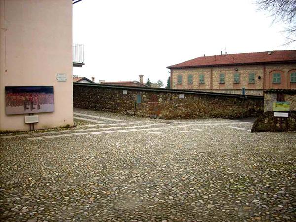 Cobblestone square with stone wall and brick building under grey sky