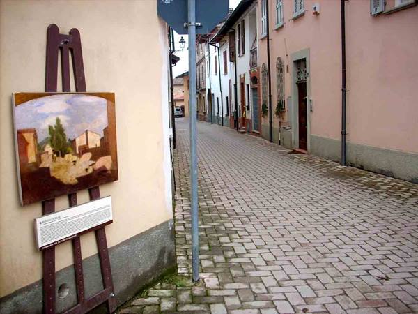 Easel with painting and plaque beside a cobbled village street