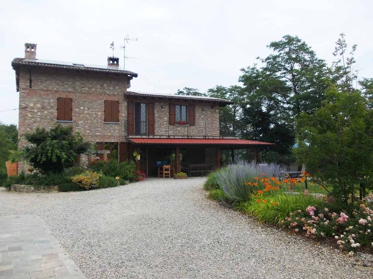 Casa rurale in pietra con tetto rosso, portico in legno e aiuole fiorite davanti