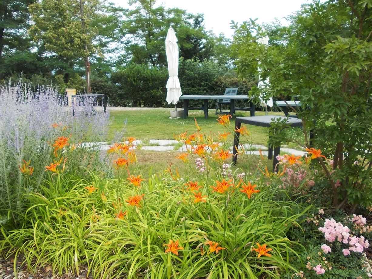 Giardino con gigli arancioni e rose, tavoli e ombrellone bianco sul prato