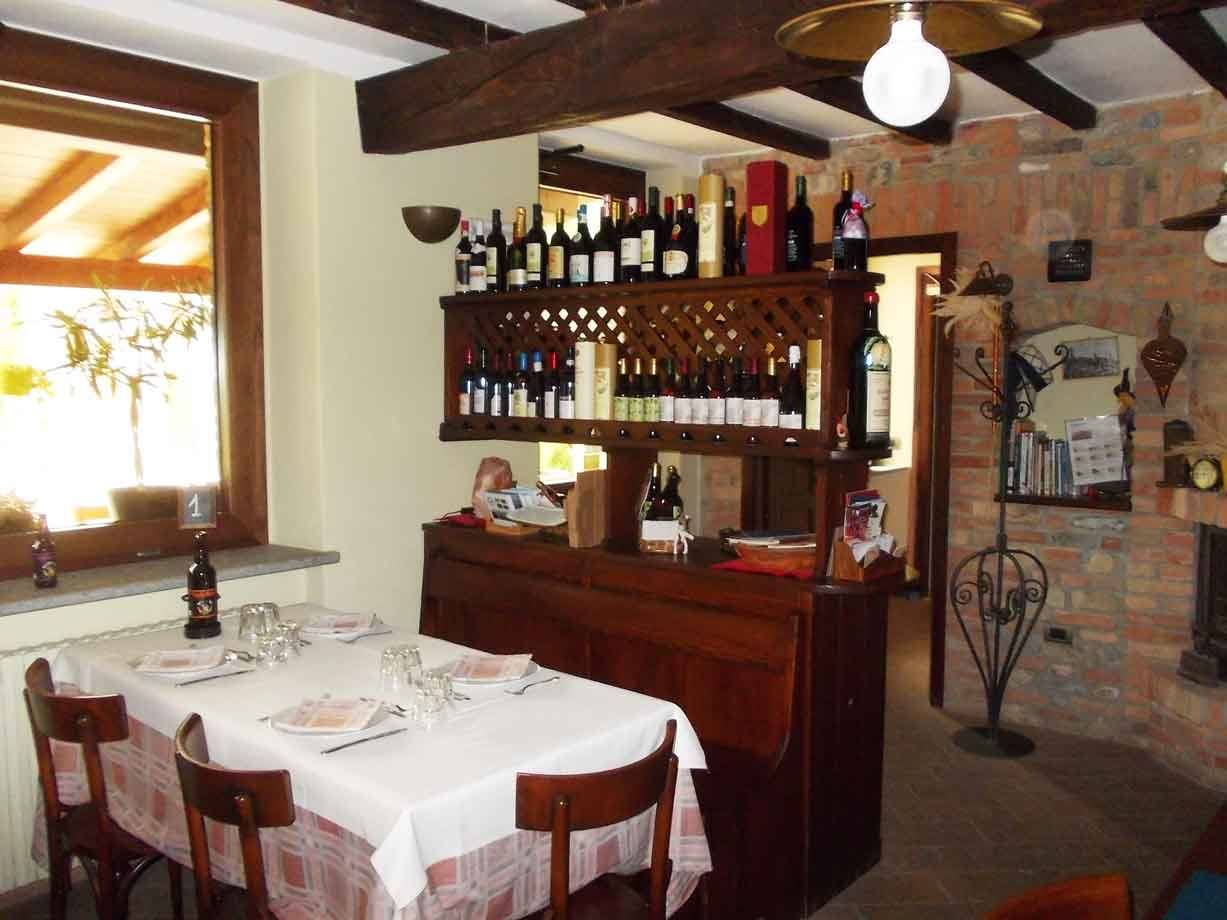 Sala di trattoria con tavola apparecchiata, scaffale di bottiglie di vino e travi in legno