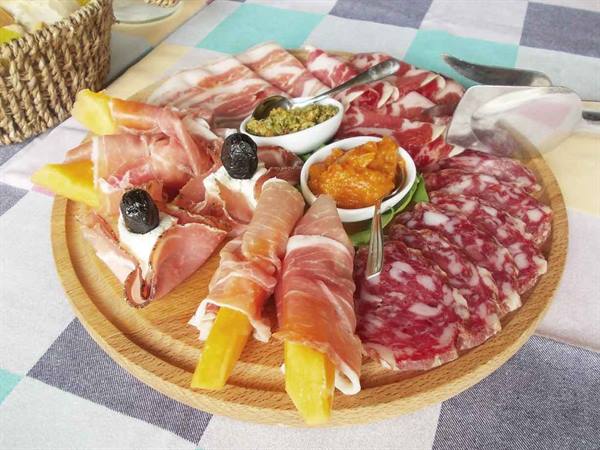 Wooden board with prosciutto, salami, melon and sauces on a checkered tablecloth
