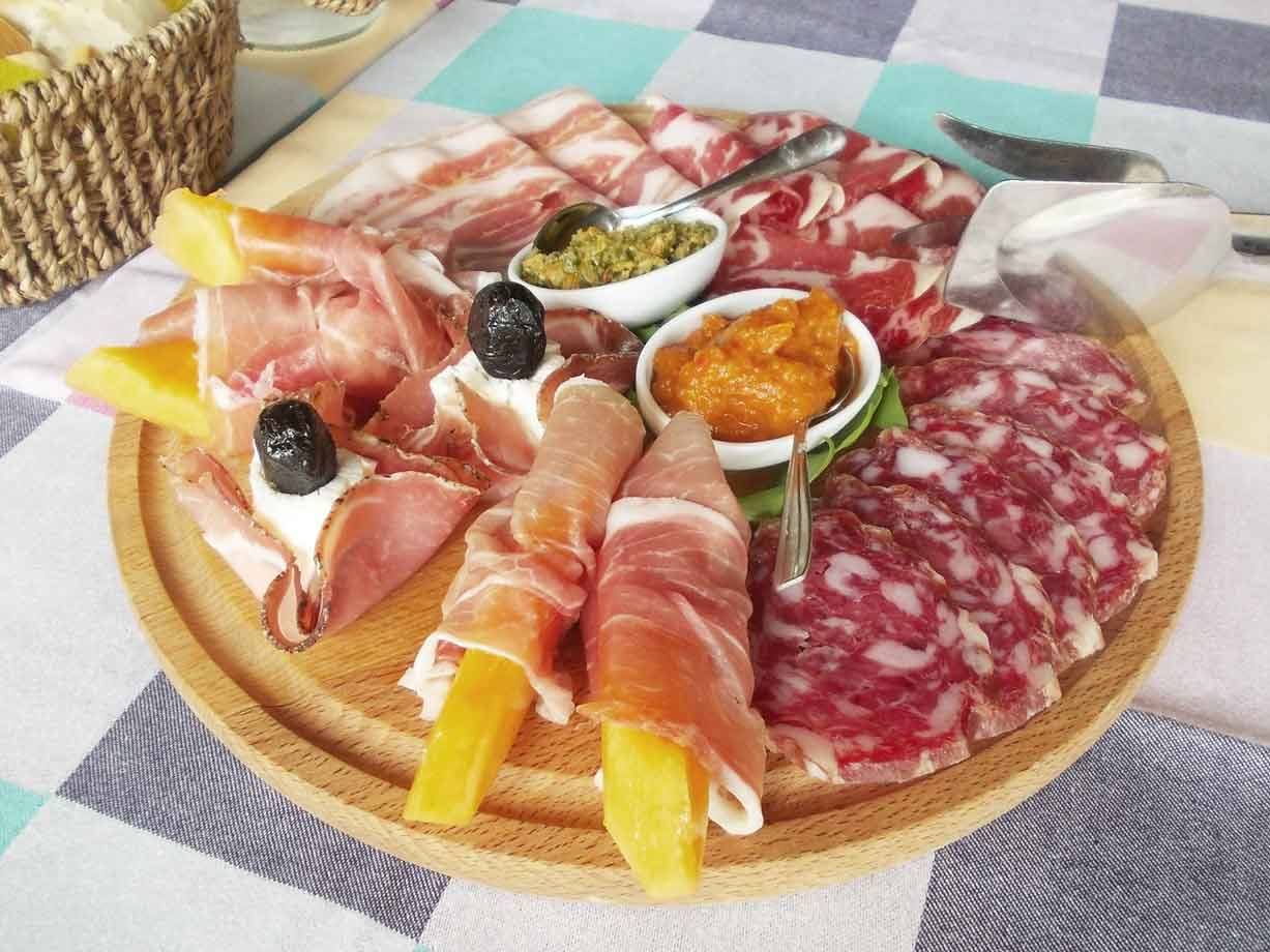 Tagliere di legno con prosciutto, salame, melone e salse, su tovaglia a quadri