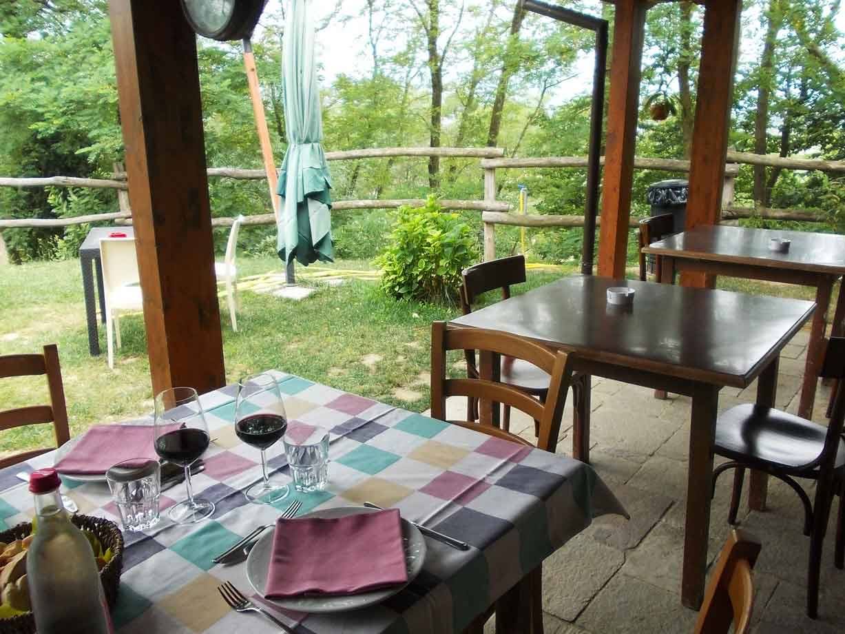 Tavola apparecchiata con vino rosso sotto il portico in legno di un agriturismo