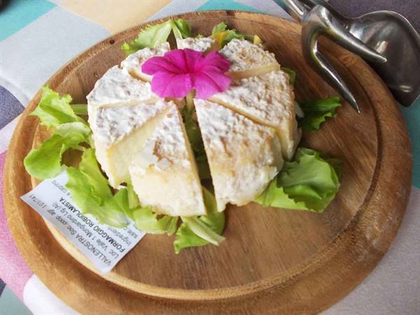 Sliced cheese wheel with pink flower and lettuce on a wooden board