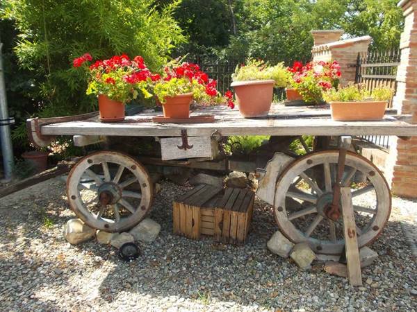 Old wooden cart with wooden wheels decorated with red geranium pots in sunlight
