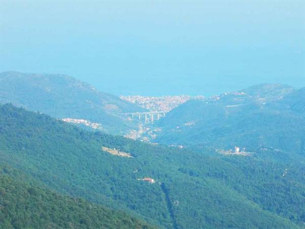 Green hills with a viaduct and a coastal town fading into blue haze