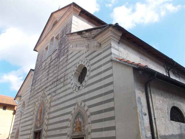 Medieval church facade with gray and white striped marble, round oculus and frescoes, cloudy sky
