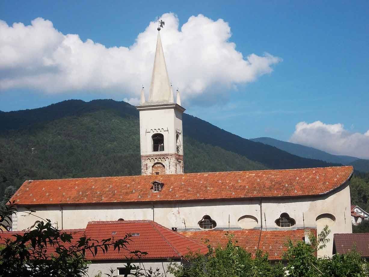 Campanile bianco con guglia sopra tetti di coppi, monti e nuvole