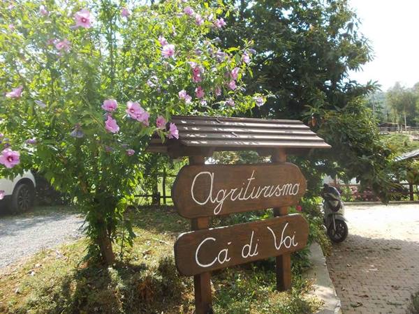 Wooden sign of Agriturismo Cà di Voi among pink flowers and a scooter