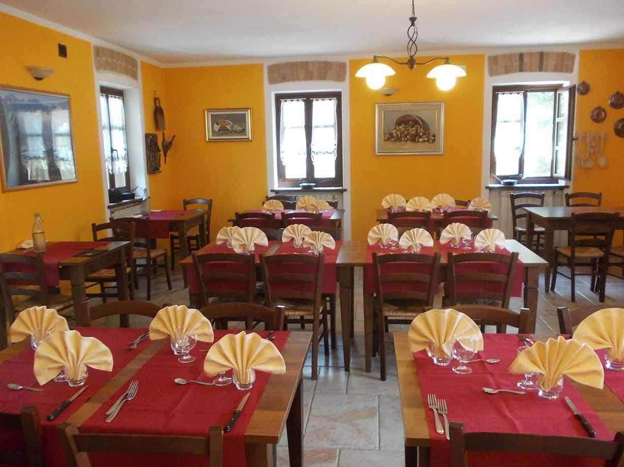 Sala da pranzo rustica con pareti gialle, tavoli apparecchiati con tovaglie rosse e tovaglioli piegati