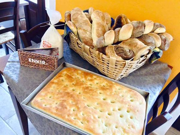 Focaccia in a tray and baskets of fresh bread on the table