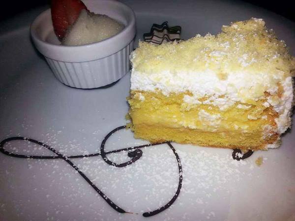 Slice of mimosa cake with cream on plate, beside small cup with strawberry and cream