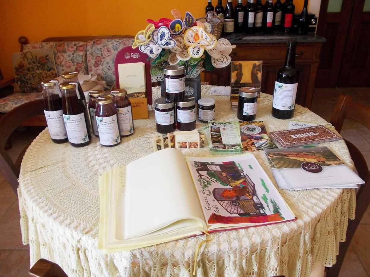 Tavola rotonda con tovaglia all'uncinetto, vasetti di marmellata, bottiglie di vino e libro aperto