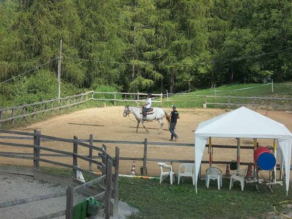 Rider on white horse in sandy riding arena, instructor walking beside, wooden fences