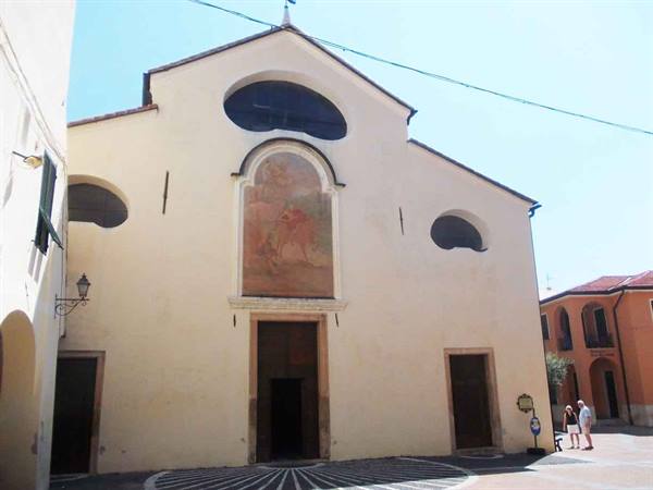 White church facade with fresco and oval windows, tourists in the square