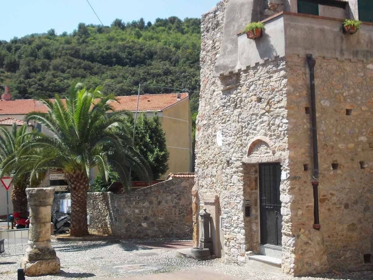 Borgo ligure con casa in pietra, palma e colonna antica sulla piazzetta