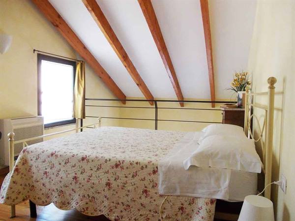 Attic bedroom with wooden beams, wrought iron bed and floral bedspread