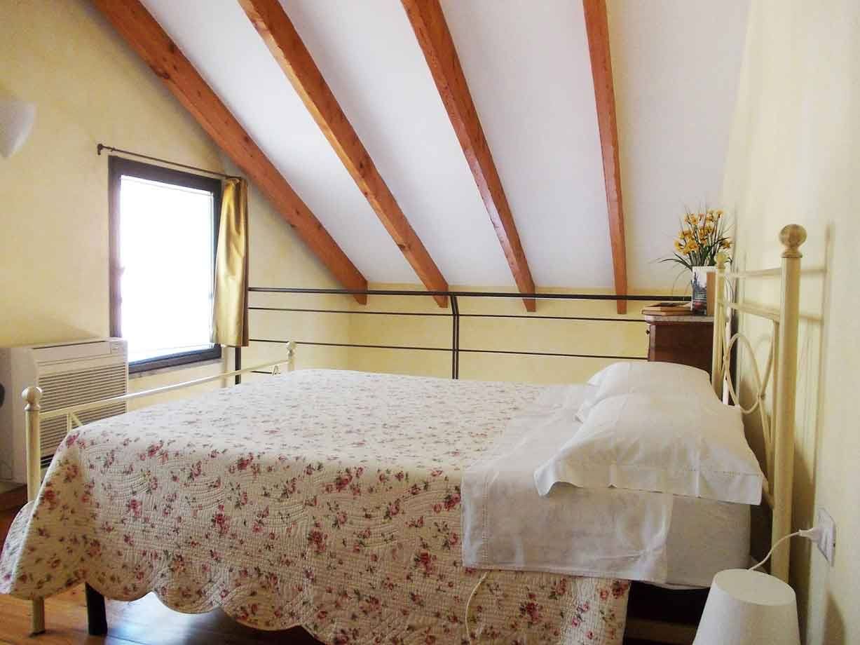 Camera da letto sottotetto con travi in legno, letto ferro battuto e copertura floreale