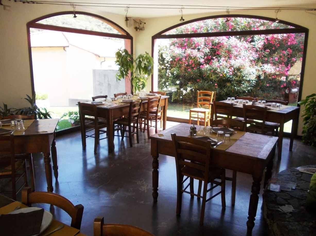 Sala di ristorante con tavoli in legno apparecchiati e grandi finestre ad arco sul giardino fiorito